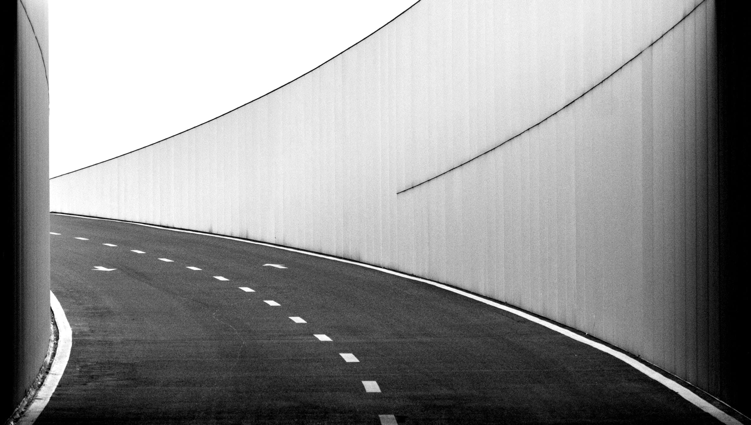 Carretera en curva con la raya central discontinua, entre muros altos.